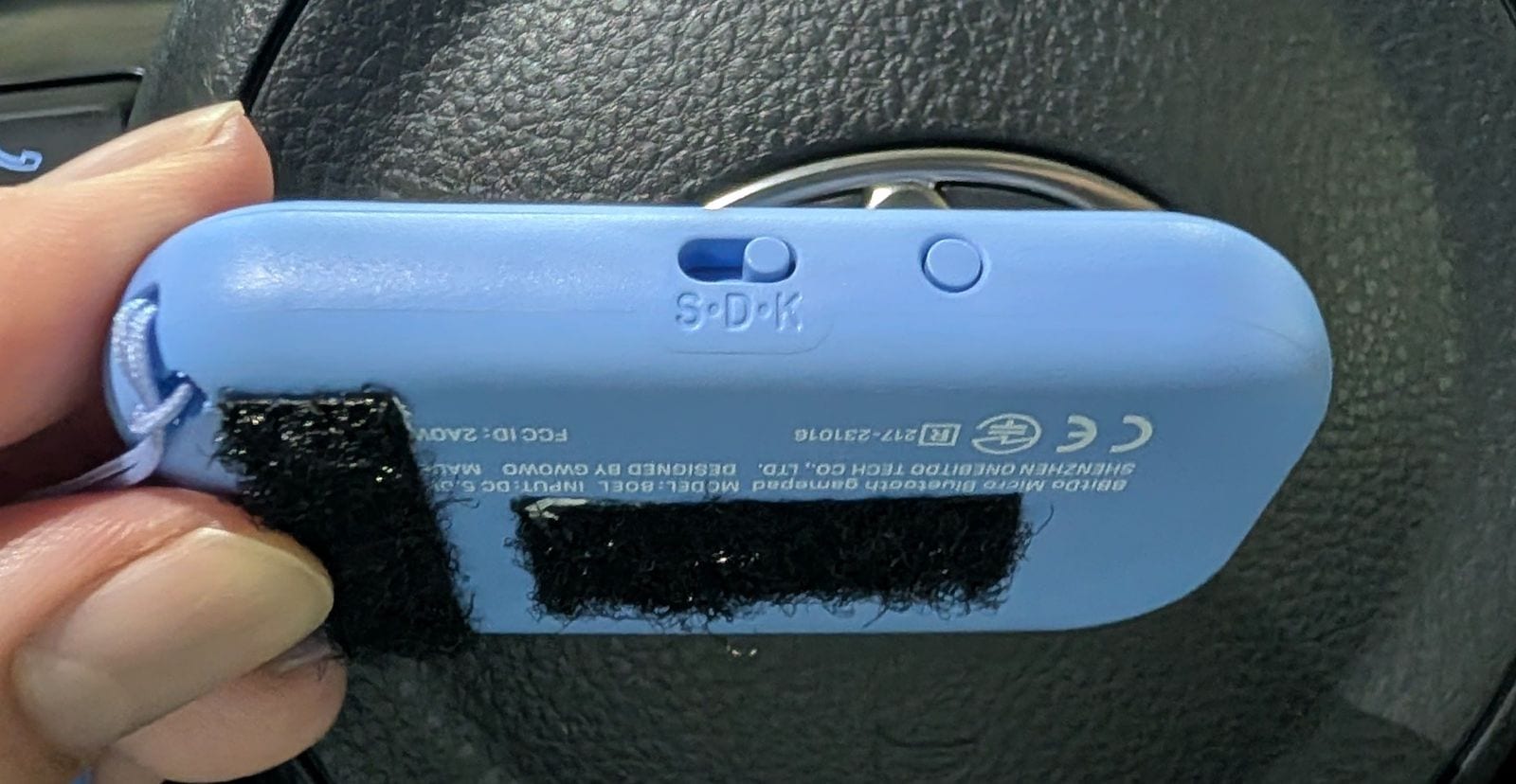 8BitDo Micro の裏面。S・D・K と刻印されたスライドスイッチと、その右にペアリングボタン。黒いマジックテープが 2 枚貼ってある
